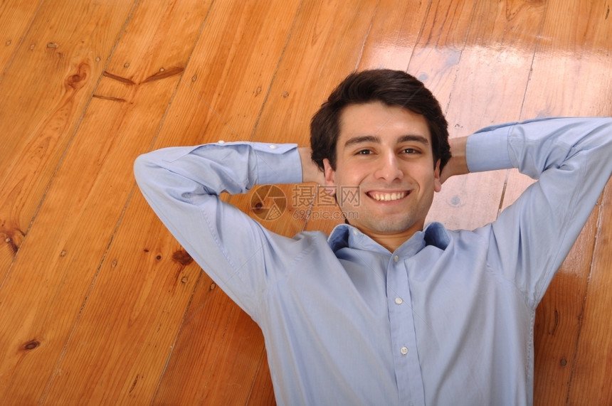年轻的蓝色在家里木地板上躺着的年轻男子他笑着有魅力的年轻男子松图片