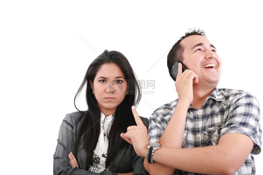 白色的妒忌女朋友站着手交叉的住院妇女看着他的男朋友在手机上听电话的男友看她朋图片