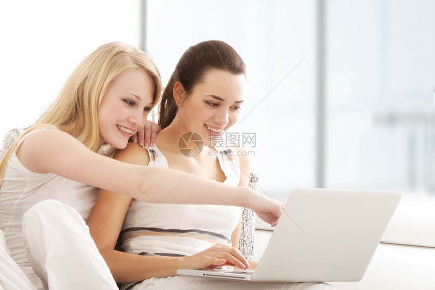 技术微笑随意的美丽年轻妇女在笔记本电脑上浏览互联网坐在客厅的索法沙发图片