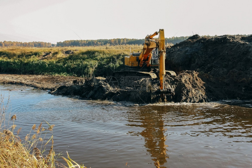 深水和清洁小河从桶里流出水的重黄色挖土机工作的跑步挖掘机图片