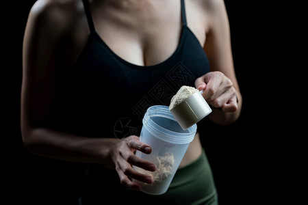 运动替换肌肉近距离接女测量一勺威氏蛋白质和摇晃瓶制作蛋白奶昔图片