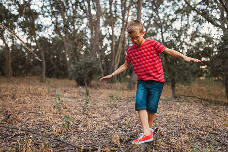 一个男孩在森林的树干上玩摇摆游戏剧孩子们衣服图片