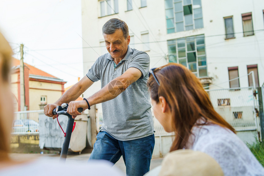 邻里家庭骑术年长男子乘电动脚踏车在夏日与附近街边妇女交谈时乘坐电踢摩托车图片