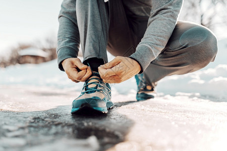 男运动鞋冷冻紧贴男人绑鞋带同时蹲守冬季健身概念图片