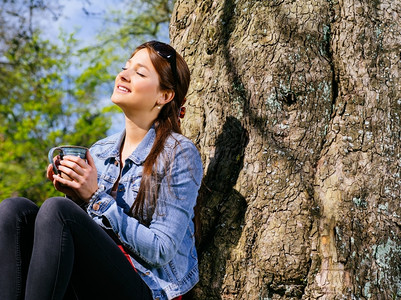 一位美丽的年轻女子在喝咖啡时享受清春初日的温暖和阳光照像公园眼睛春天图片