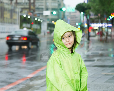 防水的漂亮穿着绿色雨衣在市街旁边淋雨的年轻女孩图片