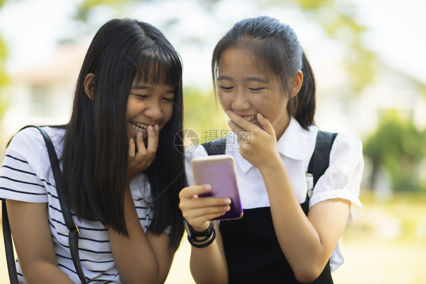 友谊幽默两个亚裔青少年笑着快乐地在智能电话屏幕上面对阅读留言聊天图片
