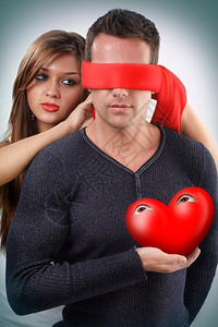 妇女蒙上一个男人的眼睛将他睁开的眼睛心放在手中礼物英俊的浪漫图片