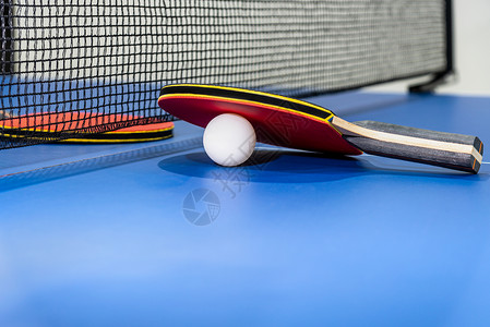 为了红桌网球拍和在蓝乒乓桌上用黑网的白球两桌板是体育竞赛设备用于室内活动以及概念背景运动红桌网球一个红桌俱乐部趣背景图片