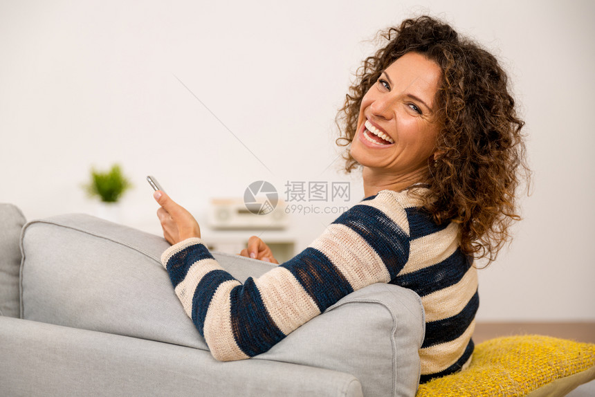 坐在沙发上笑着短信的漂亮女人在发短信时无线的联系肖像图片