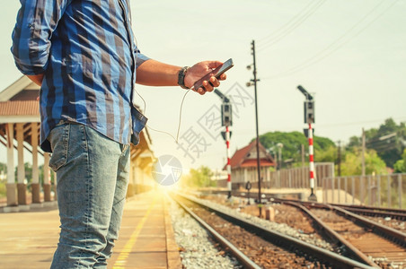 靠近蓝色的男观光客携带着智能电话耳机JP站在铁轨附近古老的音调手表图片