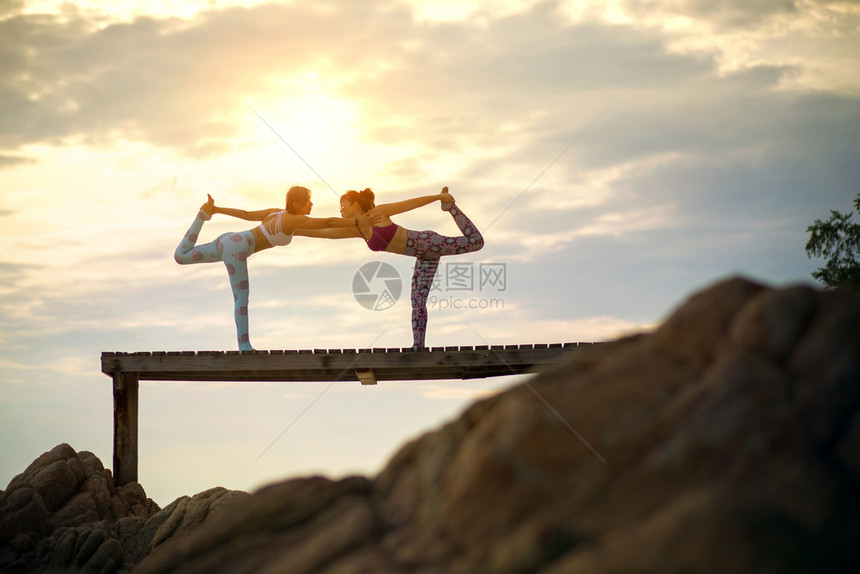 在海滩码头做瑜伽姿势阳光照耀的女子情侣运动摆姿势成人图片