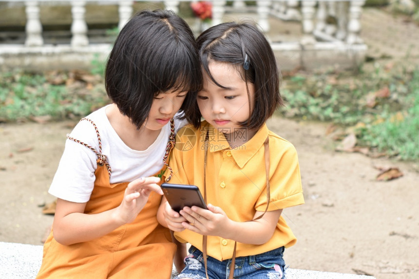 姐两个妹子女在户外公园玩智能手机游戏和幸福坐着图片