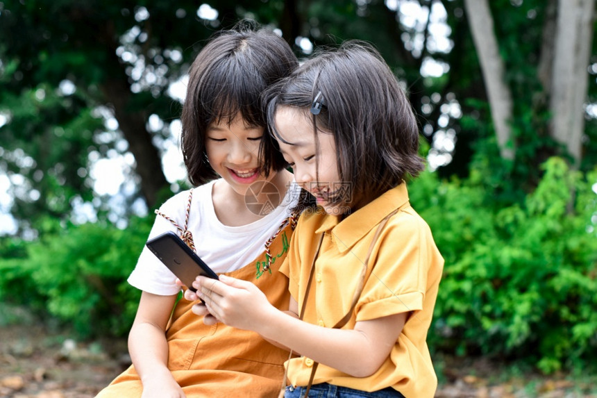 女孩两个姐妹子在户外公园玩智能手机游戏和夏天技术图片