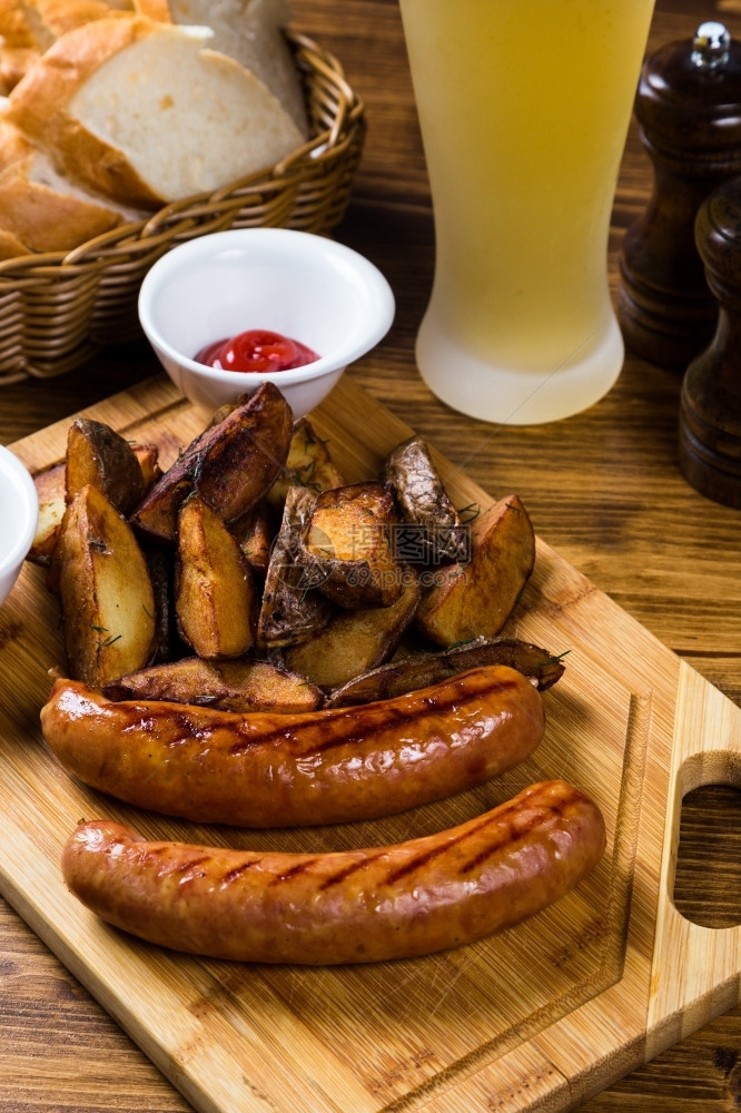 小吃慕尼黑啤酒节甘油香肠和烤土铃薯木板配香料桌上有轻啤酒番茄酱图片