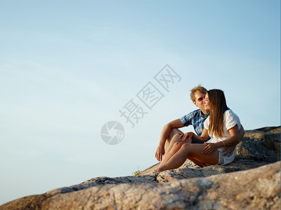 快乐的夏天小情侣坐在悬崖上蓝天坐在背景上晴图片