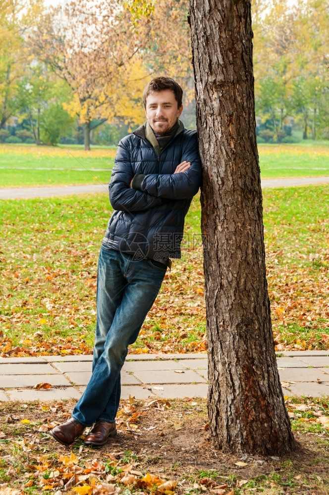 微笑帅哥靠在秋天公园的树上美丽街道图片
