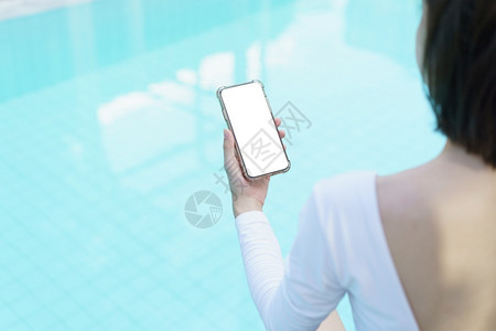 手握白屏幕手机身穿色泳衣的女在游池旁图片