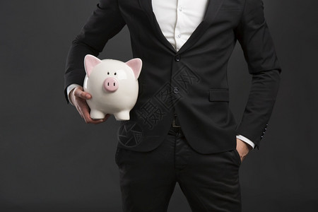 目的年轻商业穿礼服人拿着猪钱盒图片