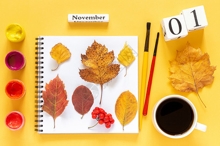 秋天你好毛笔字最佳数字秋季作文木日历1月日杯咖啡黄色背景上带有秋季彩叶和水颜料的记事本顶视图平躺概念你好月日历杯咖啡带有秋季彩叶和黄色水颜料的背景
