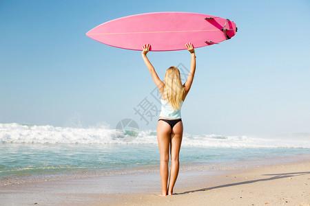 海滩上冲浪女孩高举冲浪板图片