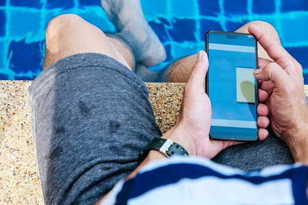 可移植在游泳池旁使用智能手机的人经过全球图片