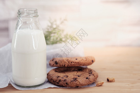 巴氏杀菌巧克力曲奇饼干和一杯牛奶在温暖的阳光下在木制桌台上乳品甜点花生背景