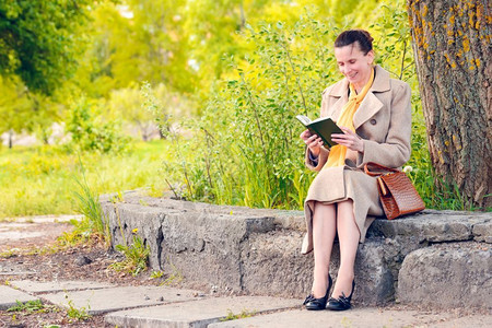 外套围巾在阳光明媚的春天坐在石墙上阅读一本有趣的书优秀女商人士图片