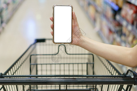 移动的部小样Mockup双手握着空白屏幕移动电话和超市购物车数字支付概念背景图片