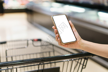 在线的技术小工具Mockup双手握着空白屏幕移动电话和超市购物车数字支付概念背景图片