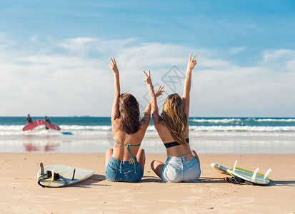 拿冲浪板女孩两个冲浪女孩在海滩上手臂张开庆祝背景