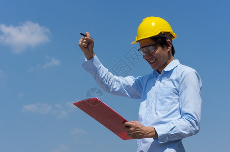 英俊的工业技术员带着黄色头盔和清单的工程师微笑表和清单图片