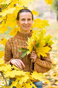 一个笑着的成年天主教女人秋在公园里采黄色的树叶子九月人们图片