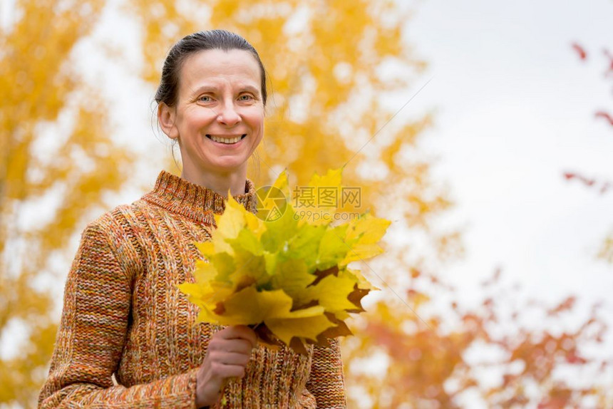 女士白种人58皮卡一个笑着的成年天主教女人秋在公园里采黄色的树叶图片