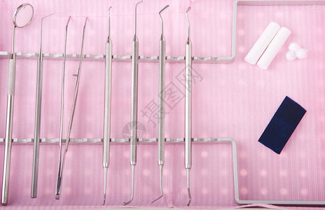 托盘中的牙科口腔包放在粉红色胸边外科器械讲义纸棉花卷和羊毛上卫生保健插件专业的背景图片