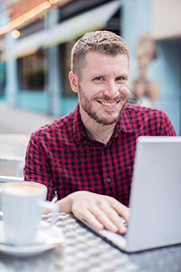 二十多岁自由职业者喝外门咖啡厅在笔记本电脑上工作的年轻人肖像图片