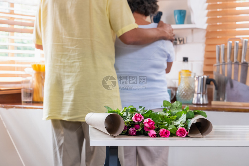 屋惊喜与亚洲高龄丈夫拥抱妻子在家中厨房餐桌上摆放花朵瓦伦蒂纳柯斯Daylovely老年情侣概念礼物图片