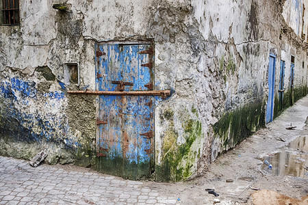 位于摩洛哥Essaouira的Mellah区一个街角的破旧的蓝色小门和一间酒吧在个破败社区里用于保安的全为了城市的蓝色背景图片