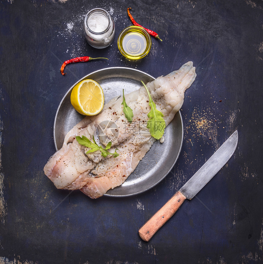 蛋白质盐生鳕鱼在一个锅里生鳕鱼上面有草药和刀子在生锈木背景上肉图片