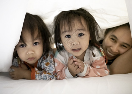 女儿可爱的亚洲家庭肖像躺在床上白色毯子下看着镜头与家人的放松时光孩子图片