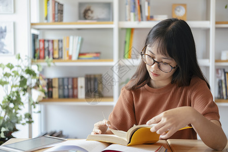 在书架前阅读书籍的戴眼镜女孩图片