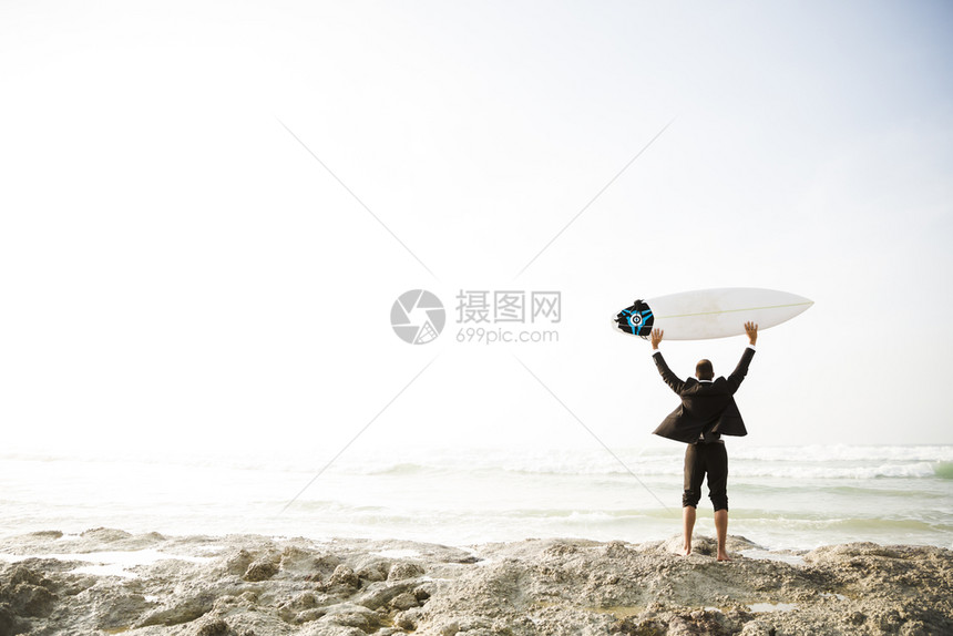 商务男士拿着冲浪板来到海边图片