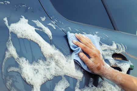 女人在肥皂泡沫中手用蓝海绵洗车水清洁器汽图片