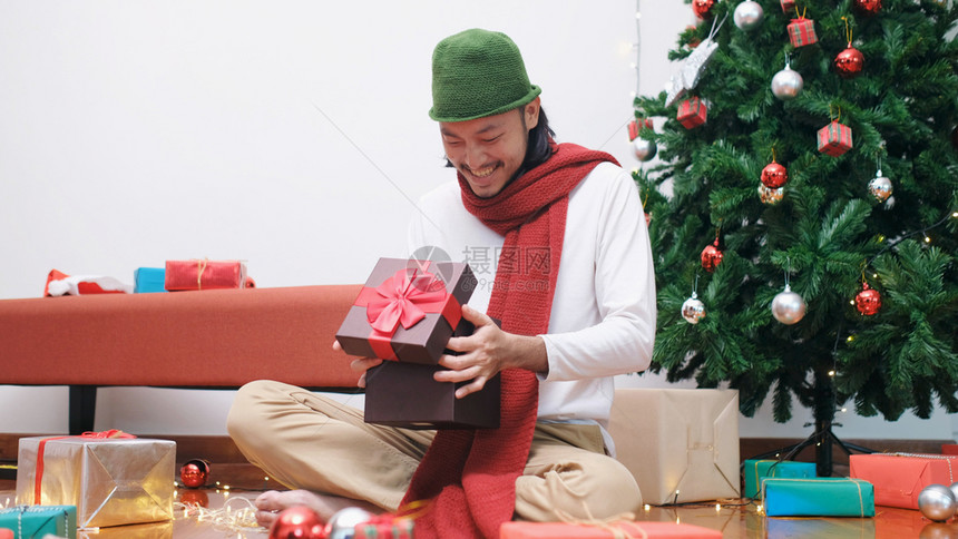 乐趣男人红色的年轻亚洲男子在圣诞节庆典晚宴上开圣诞礼物箱时带着快乐的笑容微图片