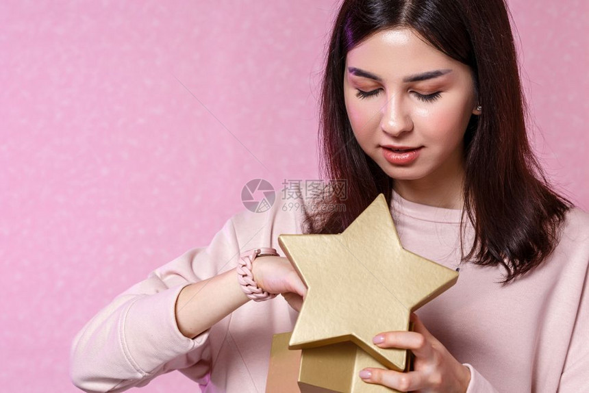 亚洲人抓住纸以金星形状的礼物盒在一位亚洲女孩手里一个粉红孤立背景的年轻亚洲女孩图片