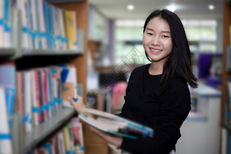 在图书馆书架前抱着书的亚洲女孩图片