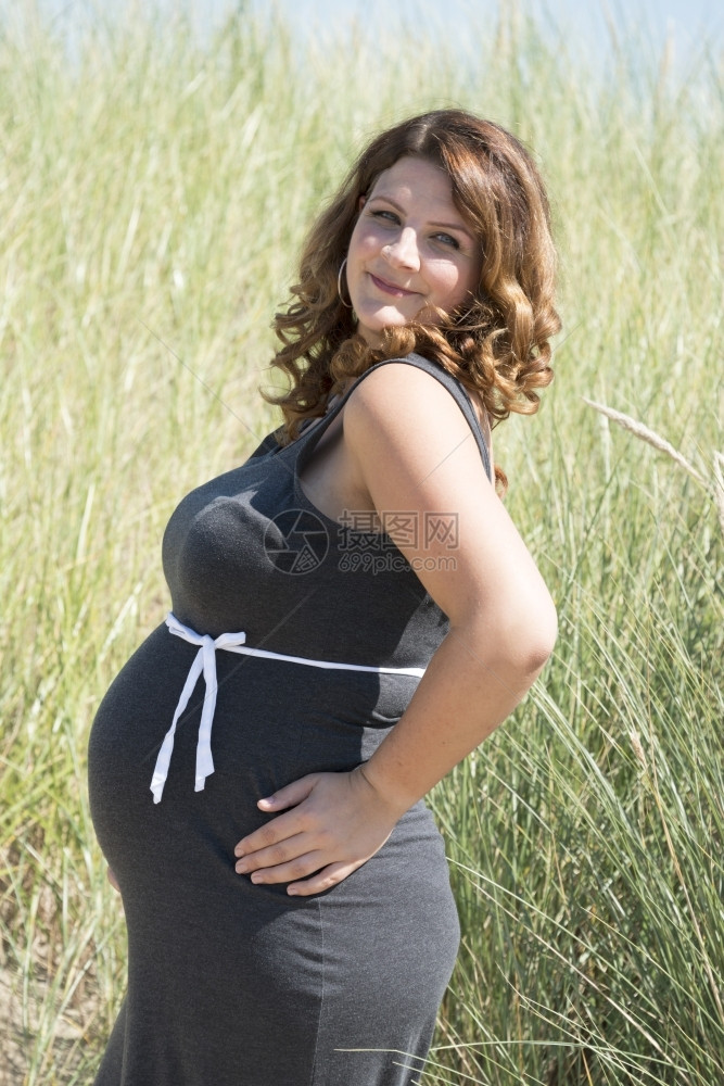 产假母亲孕妇腹部怀着白丝带弓的在大自然中有稻草背景手图片