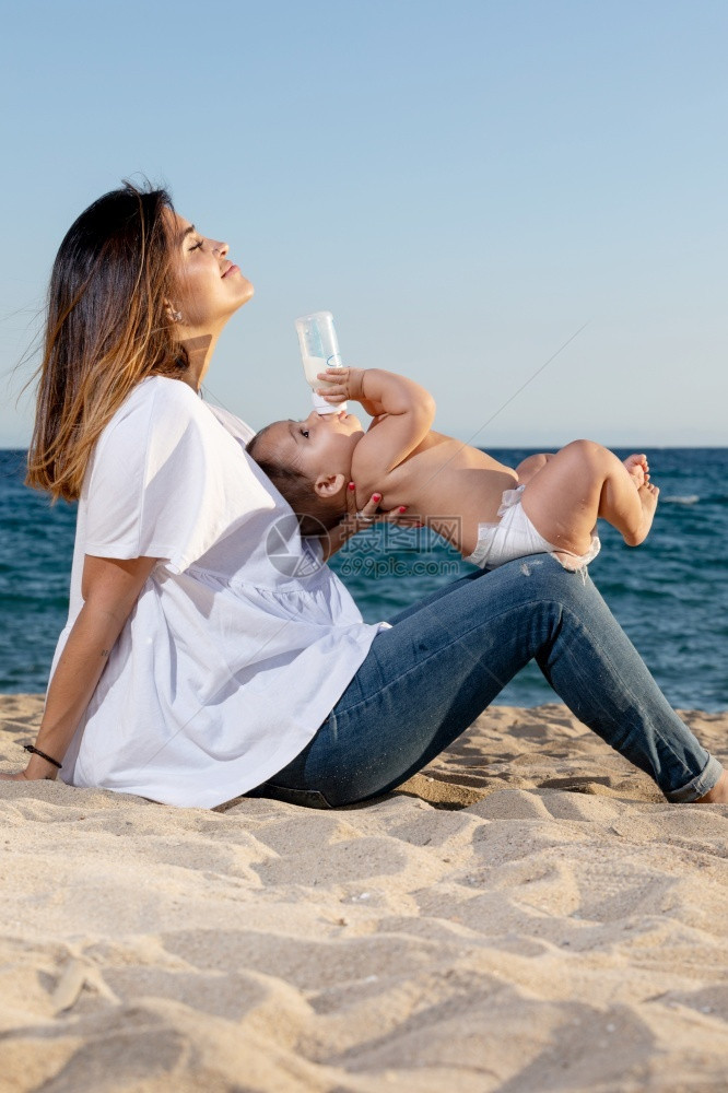 营养婴儿奶瓶中新生饮水牛奶坐在户外母亲的腿上赤脚快乐图片