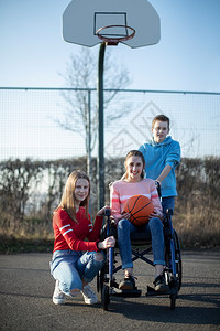 朋友们卫生保健坐在轮椅上的少女与朋友一起打篮球的肖像微笑背景图片