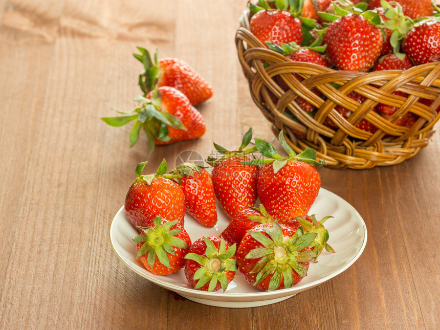 甜的白盘子里红草莓和木桌上的篮子里有新鲜红草莓木头桌子图片